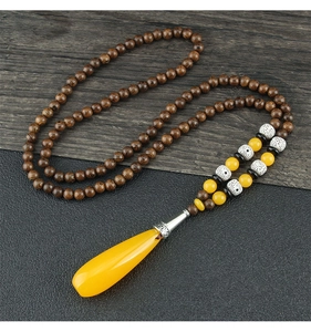 Detail of wooden bead long necklace featuring amber drop pendant on dark wood background