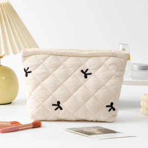 Detailed close-up of quilted cosmetic bag with black bow embroidery on cream fabric