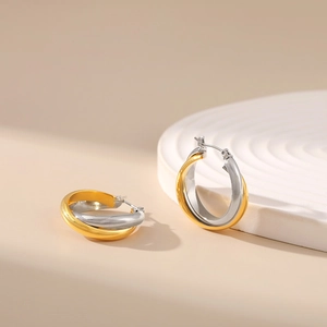Close-up of interlocking gold and silver twisted hoop earrings on a textured display stand