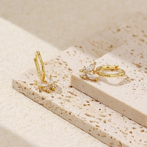 Detailansicht goldener Schmetterling-Ohrringe mit klarem Zirkon auf Steinoberfläche