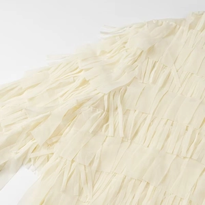 Close-up of layered fringe texture and chiffon fabric detail on ivory white blouse