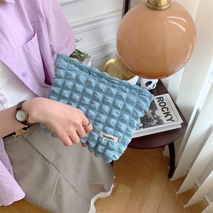 Detail of light blue bubble textured pouch with brand tag held in a cozy home setting