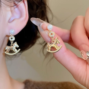 Detail of gold pearl earrings featuring horse charm and ancient coin design on model