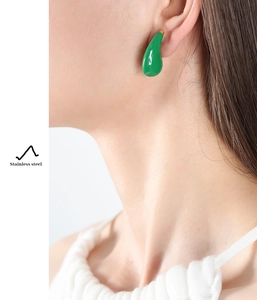 Detail of green teardrop earring in polished stainless steel worn by a model