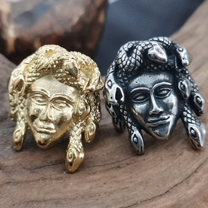 Macro shot of gold and silver Medusa head rings displayed on a rustic wood base
