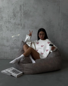 Close-up of white oversized knit sweater with pink heart pattern in a casual setting