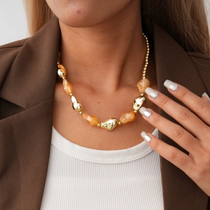 Detail of amber resin beads and gold metallic spheres on a stylish necklace worn by a model