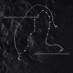 Detail of silver chain necklace with crescent moon pendant and blue beads on black stone