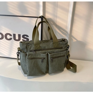 Close-up of green corduroy tote bag featuring multiple zipper pockets and adjustable straps