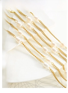 Detailed shot of golden flat chain necklace with baroque freshwater pearls on white prop