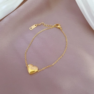 Detailed view of a gold heart charm bracelet on satin fabric showing S.STEEL engraving