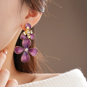 Detail of purple flower drop earrings with gold edges and crystals on female ear