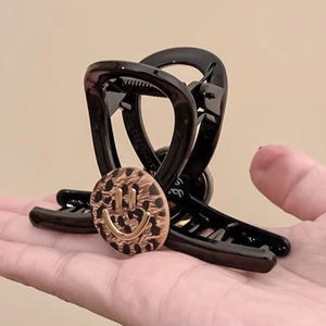 Elegant black claw clip with leopard print and golden smiley face detail held in hand