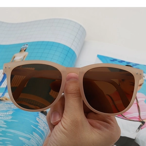Close-up of matte beige sunglasses with dark brown lenses held over a magazine background