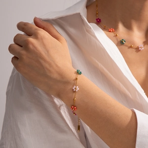 Détail du bracelet en chaîne or 18k avec breloques de fleurs colorées sur le poignet