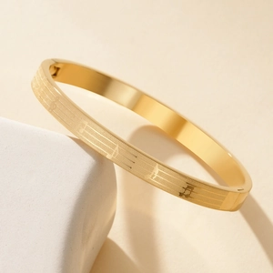 Golden titanium steel oval bangle featuring minimalist musical notes and staff engraving
