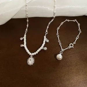 Elegant zircon flower pendant necklace and pearl bracelet set on a textured surface