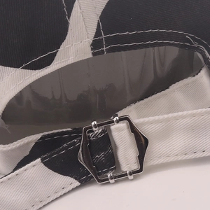 Detail of adjustable metal buckle on cow print baseball cap with white stitching