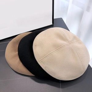 Tre baschi in lana in beige, nero e cammello esposti su un tavolo minimalista