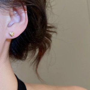 Detailed close-up of golden heart earrings with a textured hammered finish on ear