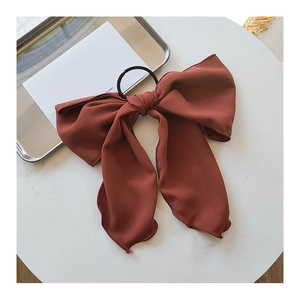 Detail of a large brick red bow hair tie made of textured fabric on a white surface