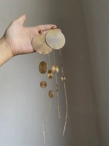 Detailed close-up of golden geometric tassel earrings with circular textured metal disks