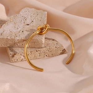 Close-up of golden knotted open cuff bracelet on beige stones and pink silk fabric