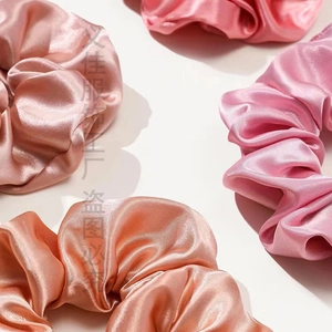 Detailed view of four glossy silk scrunchies in pink, champagne, and peach tones