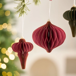 Dark red and green paper honeycomb Christmas ornaments hanging on a pine tree branch