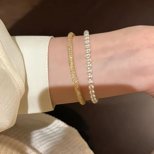Close-up of a gold micro-set zircon bangle and a white round pearl bracelet on a wrist
