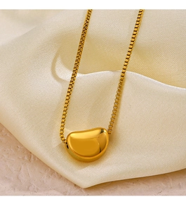 Close-up of golden bean pendant on box chain resting on soft silk fabric texture