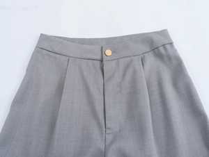 Détail du pantalon gris avec bouton doré, taille plissée et tissu tissé de haute qualité