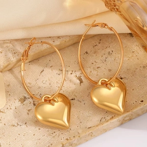 Detail shot of large golden heart-shaped hoop earrings with a mirror finish on stone surface