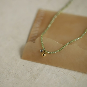 Close-up of olive green beaded necklace featuring gold and silver spherical charms