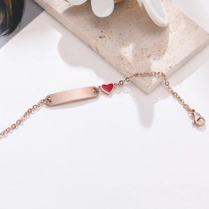 Détail d'un bracelet en or rose avec un cœur rouge et une plaque à graver en métal