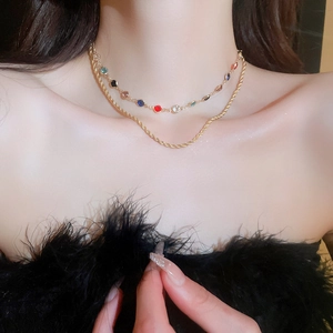 Close-up of double-layered gold necklace with colored gemstones and twisted curb chain link