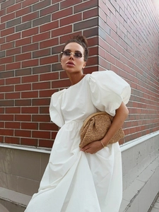 Détail d'une robe blanche en coton à manches bouffantes et pochette en paille tissée