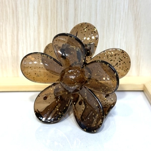 Macro view of transparent brown flower hair claw with shimmering gold glitter petals