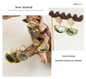 Detail view of retro gold earrings with white resin opal and green marble texture pendants