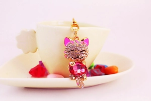 Detail of pink rhinestone lucky cat keychain with a large gemstone on a white cup