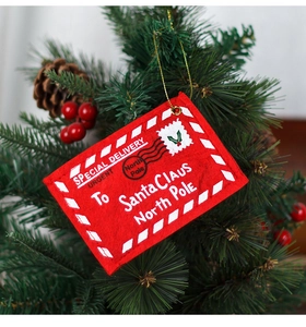 Macro detail of red felt Christmas envelope ornament hanging on a festive pine tree branch