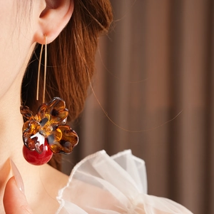 Detail view of flower-shaped leopard print earrings with red fruit pendant on model