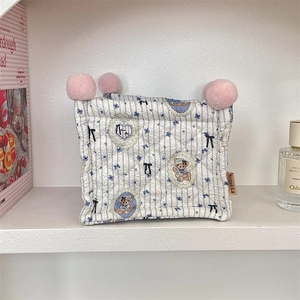 Close-up of quilted storage basket with blue stripes, floral prints and plush pom-poms