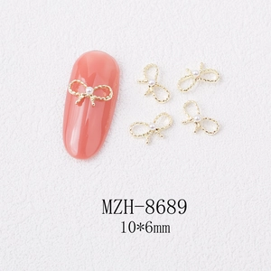 Detailed macro view of golden bow nail art charms with pearl center and rope textures