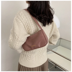 Detail of dusty pink leather underarm bag worn over an ivory cable-knit sweater