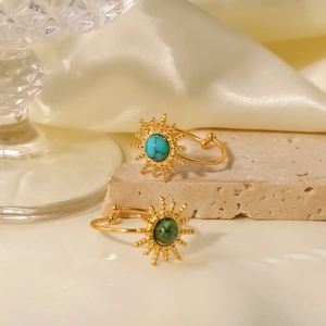 Gold sunburst open rings featuring turquoise stones displayed on a natural stone base