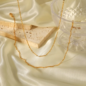 Collier chaîne bambou doré minimaliste pour femme sur fond de soie beige et de pierre
