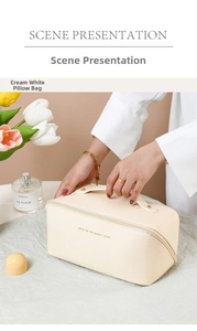Scene showing the cream white leather pillow makeup bag with top handle and golden text