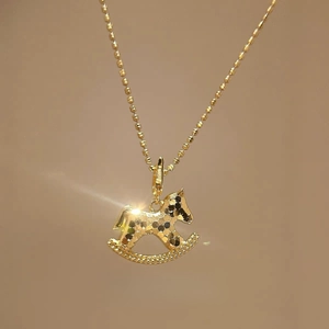 Collier élégant avec pendentif cheval à bascule doré et texture martelée sur fond beige