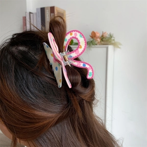 Detail of a pink butterfly hair claw with colorful polka dots on wavy brunette hair